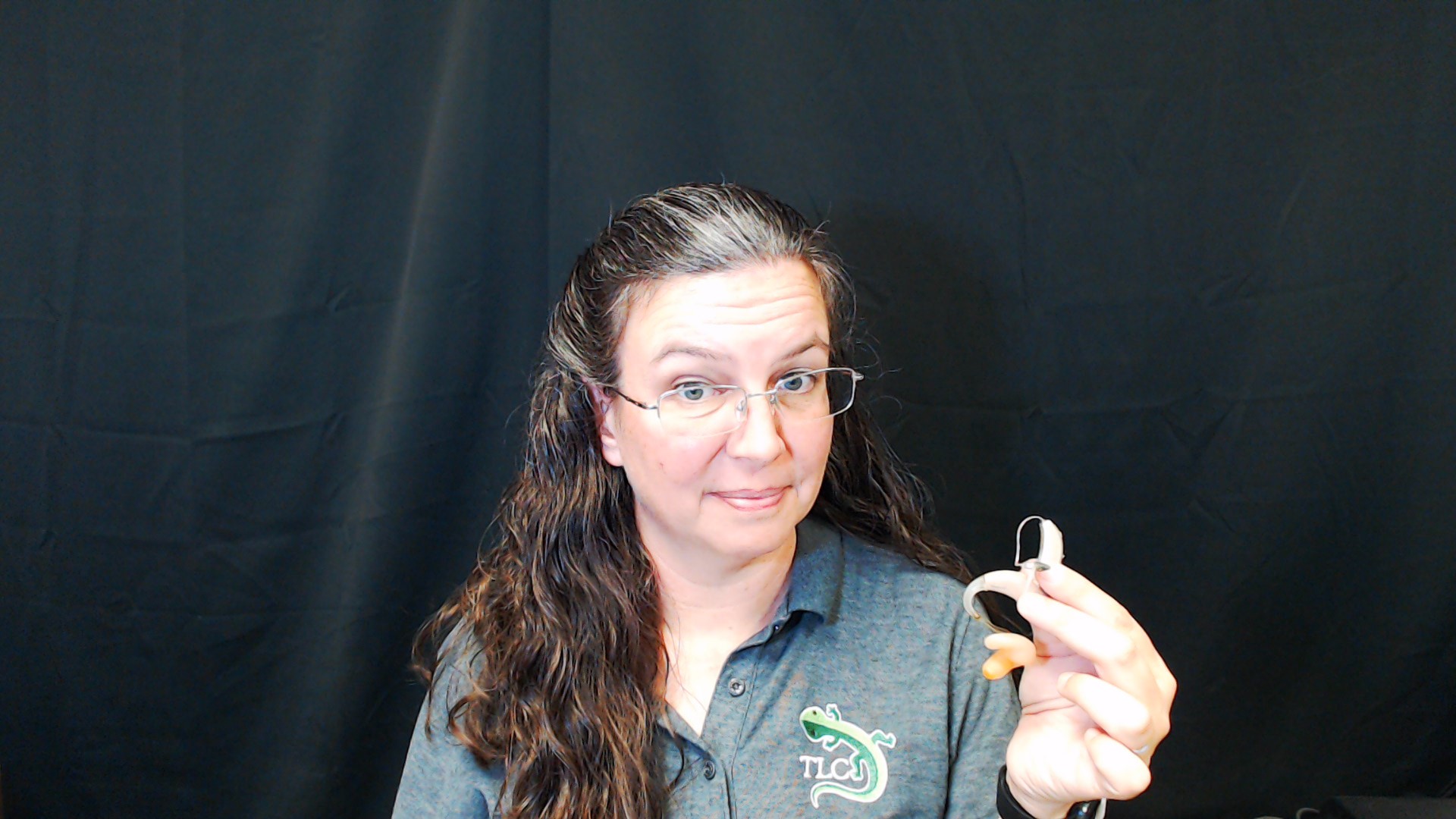 Janelle looking at camera holding two hearing aids.