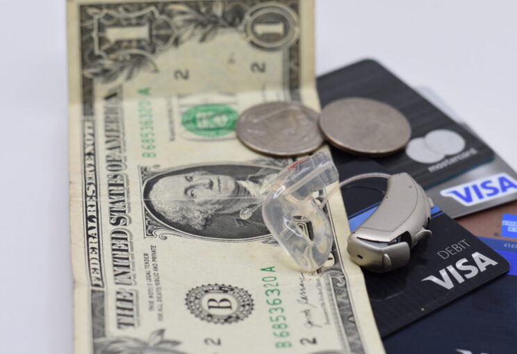 hearing aid on top of stack of credit cards with dollar bill and change.