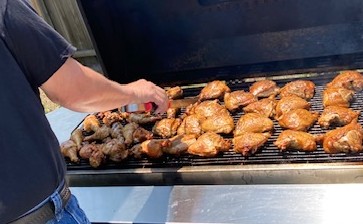 person with tongs turning chicken on gas grill