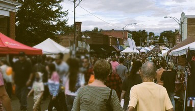 view of street fair with venders in tents and many people walking on the street