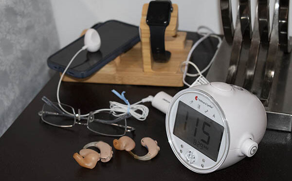 hearing aids on bedside table with glasses, cellphone, smartwatch and alarm clock