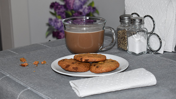 Table with napkins, salt and pepper shakers, mug with hot chocolate, plate with cookies and crumbs on the table.