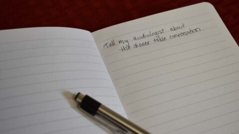 Pen and Notebook with handwritten note, tell my audiologist about the dinner table conversation