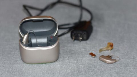 Hearing aid beside batteries and hearing aid in with cord laying on the table