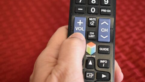 hand holding remote control. thumb on vol down button