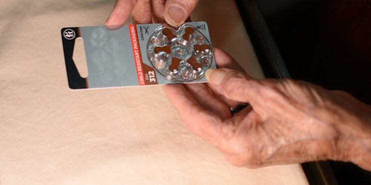 older adult hands holding a hearing aid battery package