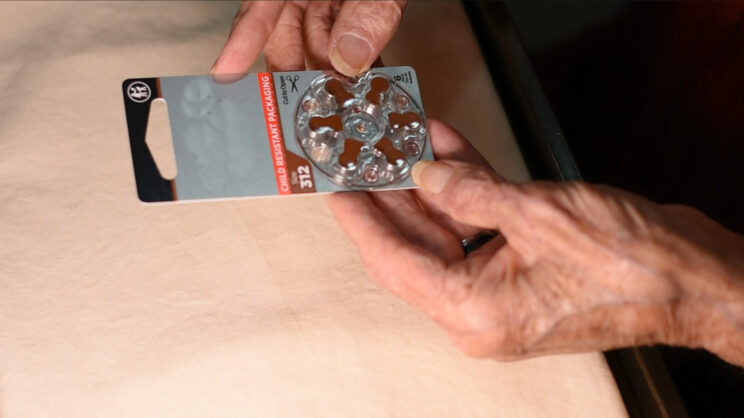 older adult hands holding a hearing aid battery package